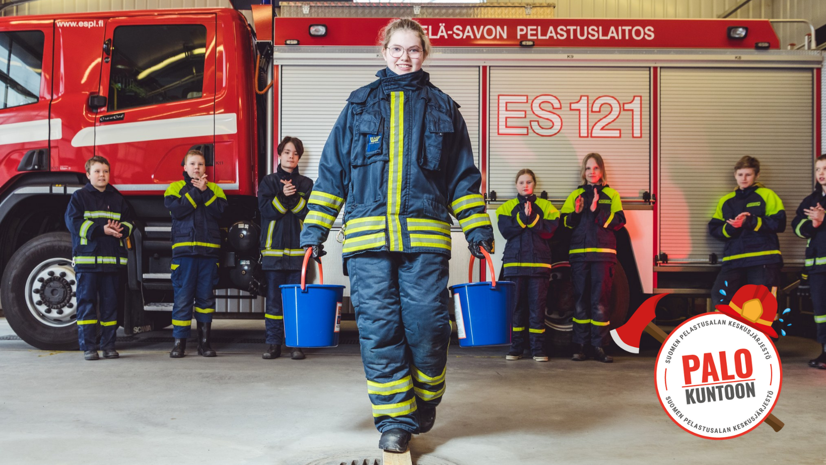 Kuvassa palokuntanuoria, joista yksi tasapainoilee laudalla kahden vesiämpärin kanssa